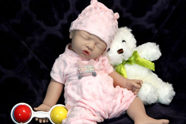 A baby doll sits beside a teddy bear and a colorful toy, creating a charming and playful scene.
